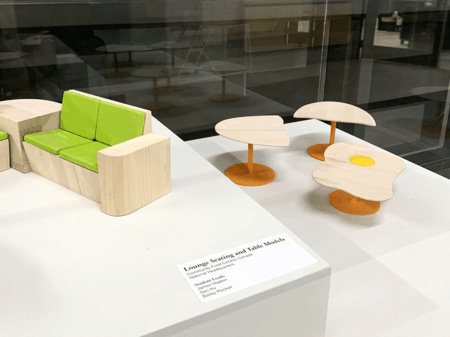 <b>Lounge Seating and Table Models</b><br>The model originates from the Sheridan Crafts and Design building.This model features a combination of natural wood and vibrant green cushions, showcasing a clean and modern aesthetic. The smooth texture of the wood contrasts nicely with the soft fabric of the cushions, creating a comfortable and inviting look. The use of bright orange for the table bases adds a playful touch to the overall design.