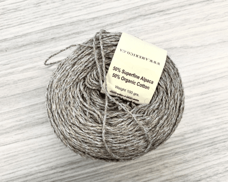<b>Yarn Ball</b><br>This yarn ball is made from a blend of 50% superfine alpaca and 50% organic cotton, showcasing a soft and cozy texture. The natural color and slight sheen highlight the quality of the fibers, making it inviting for crafting. The attached label adds a touch of detail, informing about the material composition.