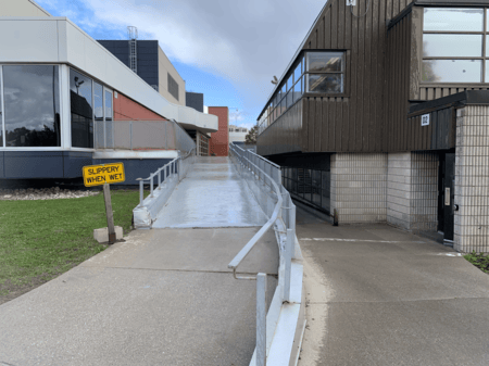 <b>OAccessibility Ramp with Caution Sign</b><br>I captured this image of an accessibility ramp on Sheridan campus with my phone. The ramp was built to ensure easy access to the buildings, especially for those with mobility challenges. It continues to serve this purpose, particularly during wet conditions, as indicated by the ‘Slippery When Wet’ sign.