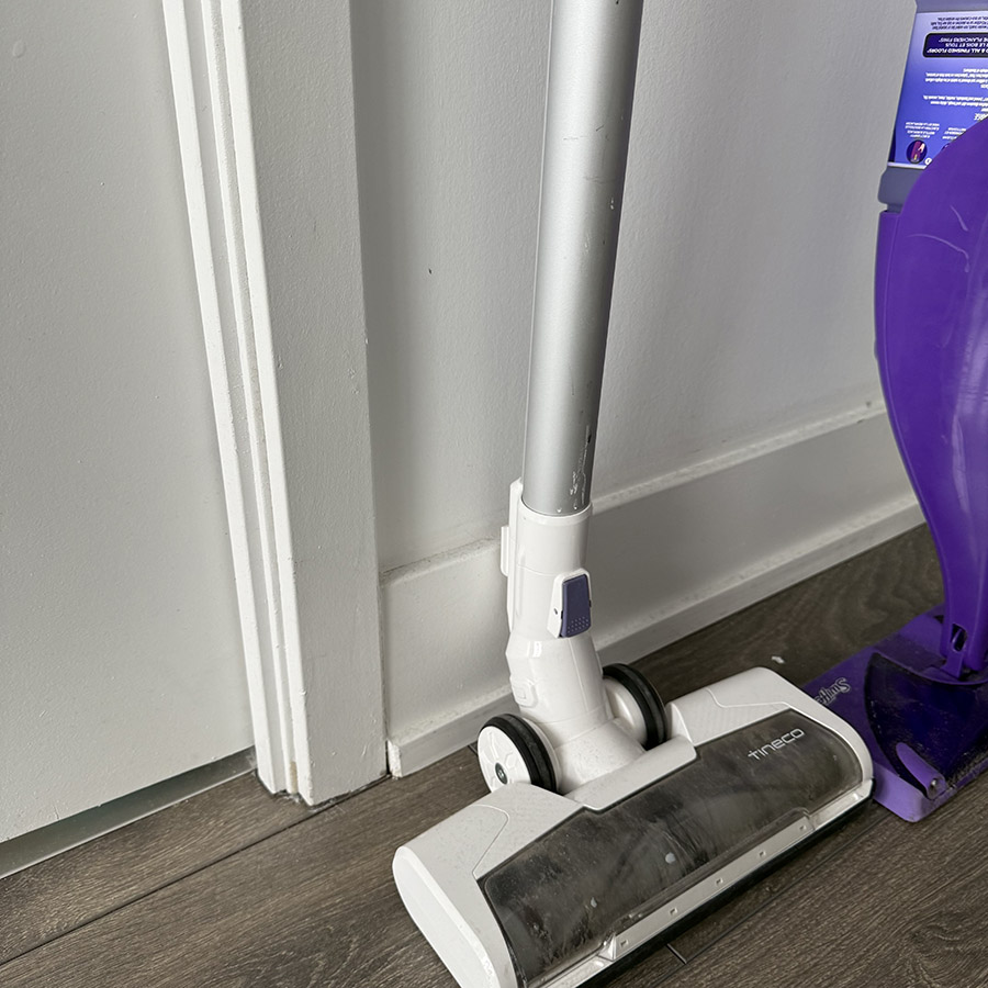 A vacuum cleaner at work near the base of a white wall, emphasizing the whirr and suction noise while cleaning.