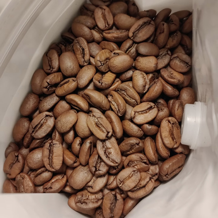 Fresh coffee beans in a grinder, ready to be ground, highlighting the crushing and grinding sounds typical of coffee preparation.