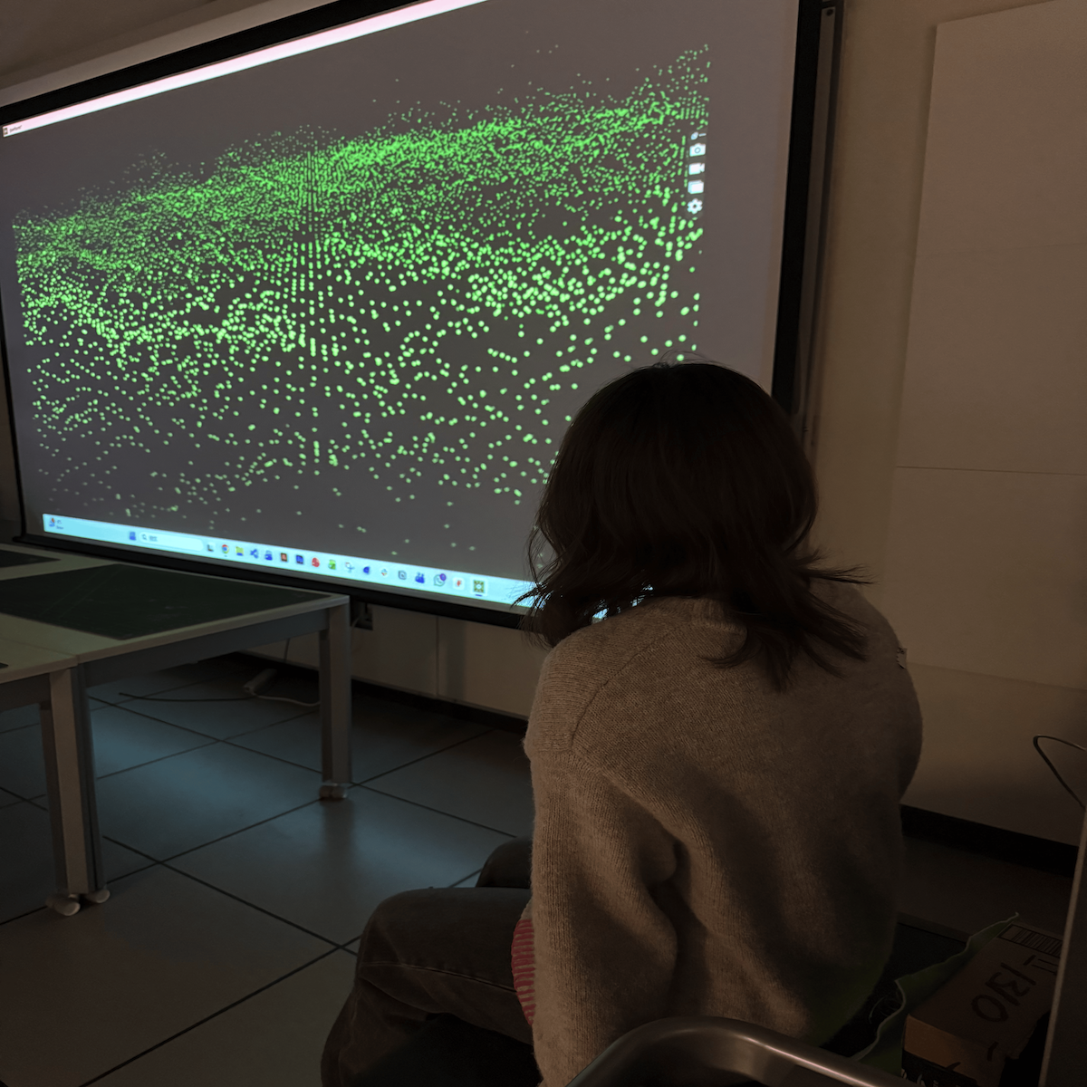 <b>User Experiencing the Projection</b><br>We tested the visuals in a real space with a full-size projection. The user sat in front of the screen while the particle animation responded to the sensor values. This photo shows the relaxing atmosphere we aimed to create.